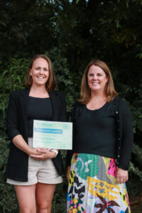 two women stand beside each other, the woman on the right holds a certificate and the woman on the right wears a colourful skirt