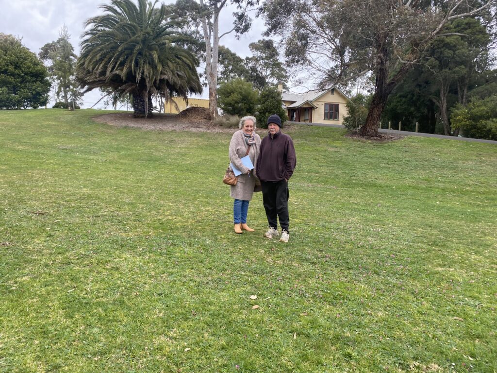 two women stand in a large grassy area, with palm trees in the background