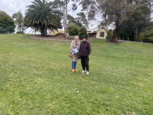 two women stand in a large grassy area, with palm trees in the background