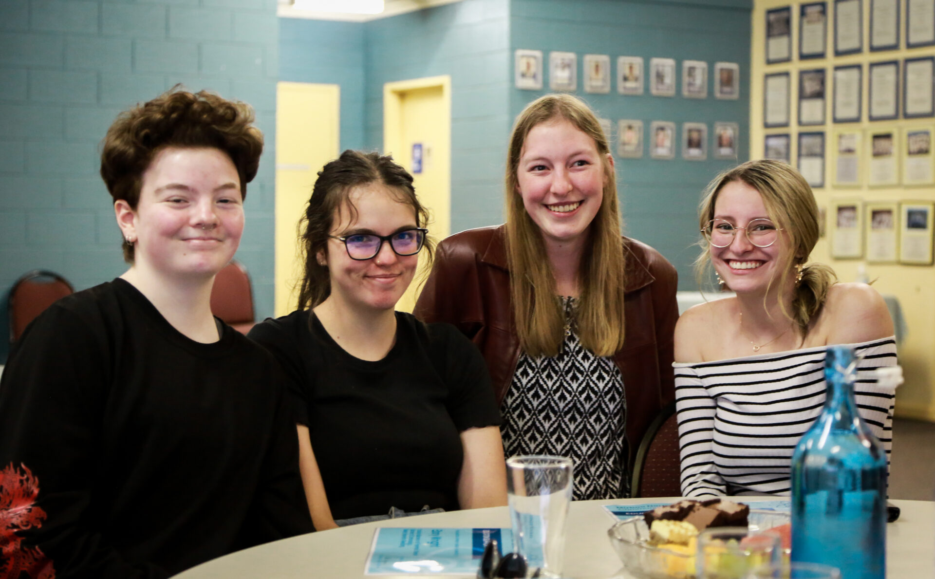 A group of young adults sit in a line at a table smiling