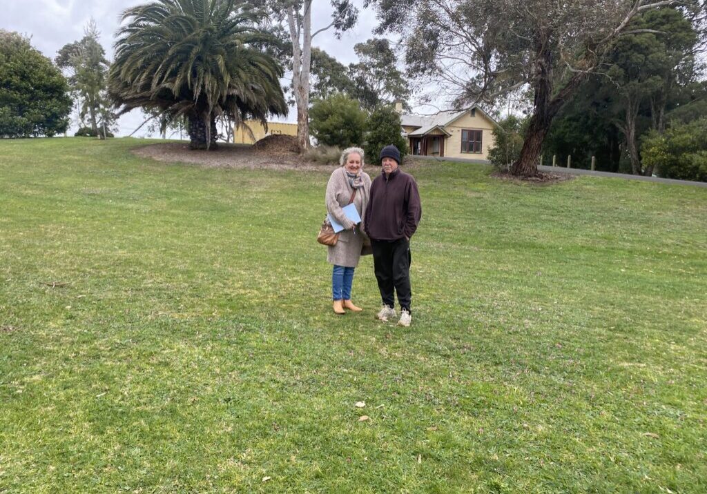 two women stand in a large grassy area, with palm trees in the background